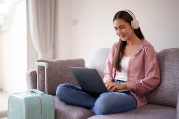Young Asian adult woman traveler prepares journey online uses laptop headphones for remote work...