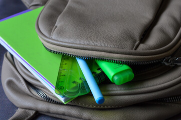 open backpack with school supplies: green notebook, ruler, pen, and highlighter. themes: education, back to school, student life, learning, stationery.