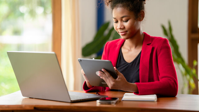 Young African American Woman Working on Tablet and Laptop in Home Office Red Blazer Business Casual Attire Remote Work Digital Device Technology