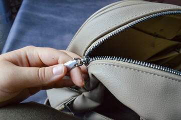 hand closing zipper on beige leather backpack. themes: travel, preparation, storage, security, packing, personal belongings.