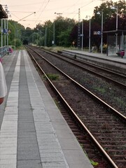Naklejka premium Gerade Bahngleise neben einem leeren Bahnsteig unter leicht bewölktem Himmel – ruhige Verkehrsszene im Regionalverkehr.