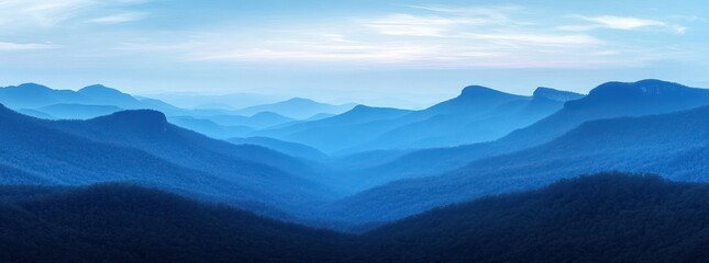 Expansive layered blue mountain ranges beneath a partly cloudy sky, evoking calm and serenity in a vast natural landscape
