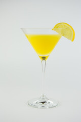 An orange cocktail in a classic martinin glass with a wedge of lemon set against a white background.