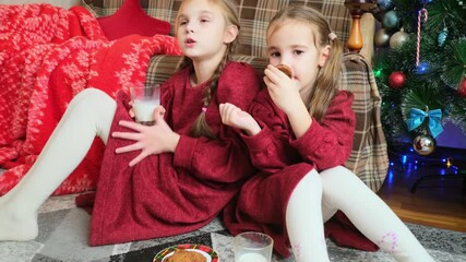 Cute little kids on eve Christmas drinking milk and eating delicious cookies at home. New Year concept