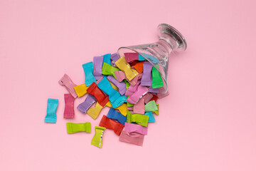 Vibrant Assorted Wrappers Spilling from Glass on Pastel Pink Background