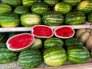A Large Pile Of Whole Watermelons At A Market Stall With Cut Samples In The Foreground To Attract Customers. Fresh Harvest Display.