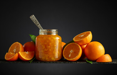 Orange jam in glass jar and fresh fruits on a black background.