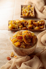 Yellow sultana raisins in a wooden bowl on a beige background.