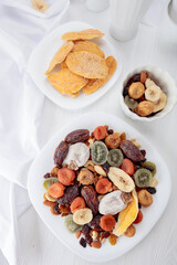 Mix of dried tropical fruits, nuts, and raisins on a white table.