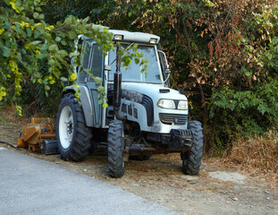 Fototapeta premium Old tractor with cleaning equipment stands in bushes after working day. Concept transport, city life