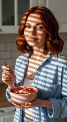 A woman with red hair enjoying a healthy breakfast of oatmeal and strawberries in her sunny kitchen.