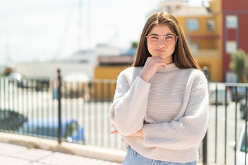 Young pretty caucasian woman with glasses at outdoors thinking