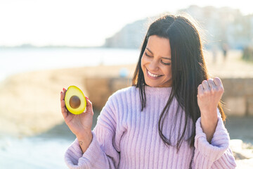 Young woman at outdoors holding an avocado at outdoors celebrating a victory