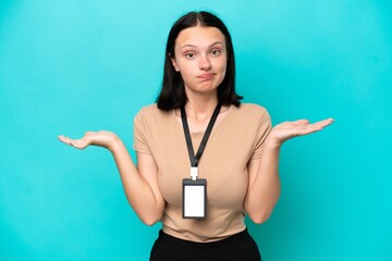 Young caucasian woman with ID card isolated on blue background having doubts while raising hands