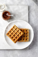 Belgian waffles empty on white plate and marble board with chocolate paste. Top view