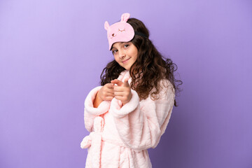 Little caucasian girl in pajamas isolated on purple background points finger at you with a confident expression