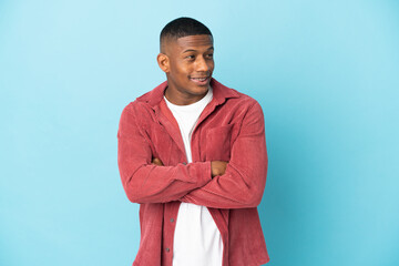 Young latin man isolated on blue background looking to the side and smiling