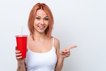 Young Russian woman holding soft drink isolated on white background surprised and pointing finger...