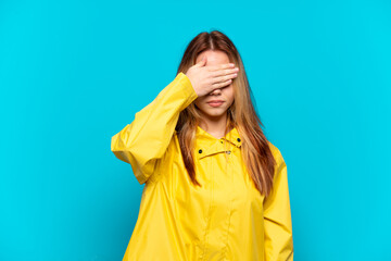Teenager girl wearing a rainproof coat over isolated blue background covering eyes by hands. Do not...