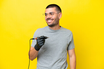 Tattoo artist caucasian man isolated on yellow background looking to the side and smiling