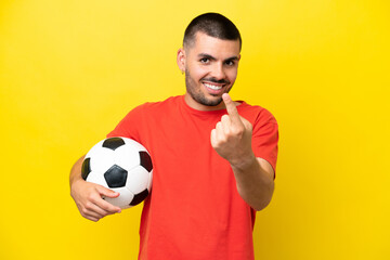 Young caucasian man playing soccer isolated on yellow background doing coming gesture