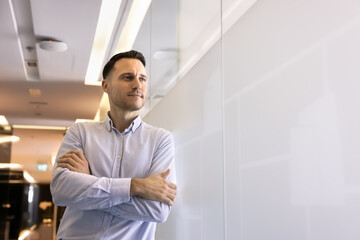 Serious thoughtful ambitious Hispanic businessman standing in office hall with hands folded at...