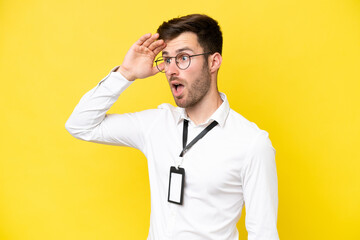 Young caucasian with ID card isolated on yellow background doing surprise gesture while looking to...