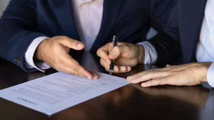 Cropped shot of two male business partners signing contract at workplace table. Businessman buying company, startup. Legal advisor, financial consultant giving support to customer with closing deal