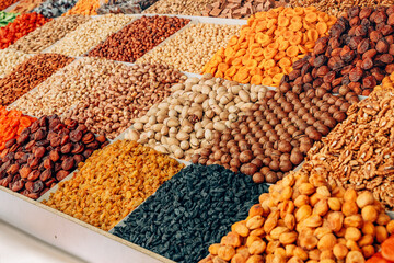 Colorful dried fruits and nuts are displayed in small wooden boxes at a market stall, creating a...