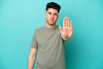 Young caucasian man isolated on blue background making stop gesture