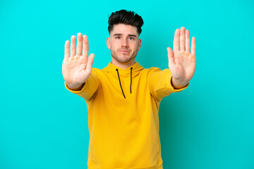 Young caucasian man isolated on blue background making stop gesture and disappointed
