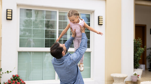 Family spend joyful life moments together outdoors. Father holding his daughter high in air, while cute kid girl laughing, exuding joy, enjoy game. Connection between dad and child, happy fatherhood