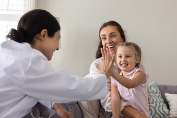 Happy Indian woman pediatrician in uniform gives high five to cute little 3s girl, kid smiling...