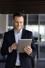 Happy young Latin businessman typing on tablet computer, using online trading service, financial...