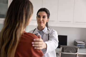Positive satisfied young Latin doctor woman touching shoulder of patient with support, discussing...