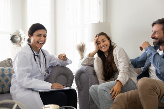 Healthcare professional in uniform and attractive married couple laughing seated together on sofa during home visit or appointment in clinic office, engaged in consultation, enjoy friendly interaction - Powered by Adobe