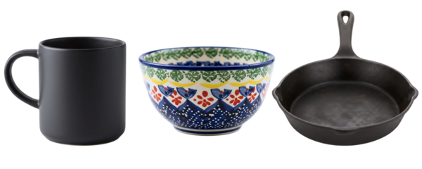 A set of rustic and artisanal kitchenware, featuring a black mug, a decorative blue bowl, and a cast iron frying pan. This collection has a charming, handcrafted, and traditional feel.
