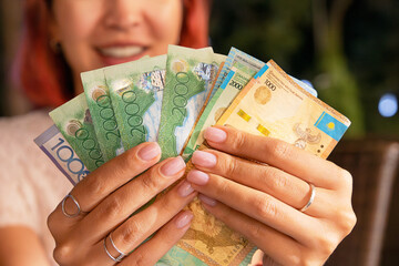 Woman showing Kazakhstani tenge banknotes with a smiling face in the background out of focus