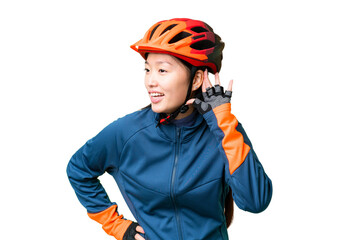 Young cyclist woman over isolated chroma key background listening to something by putting hand on the ear