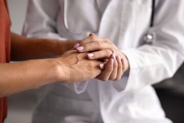 Young doctor woman holding hands of patient, making supportive gesture, giving compassion, empathy, hope, comfort, encouraging for difficult treatment, therapy. Close up dropped shot