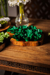 Elegant party sweets in emerald green wrappers on a rustic heart-shaped wood slice for a wedding...