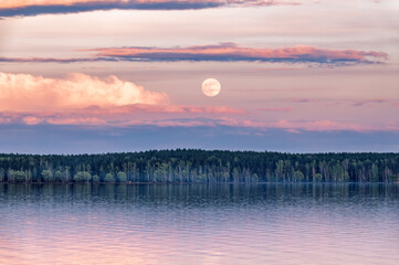 A lake with a cloudy sky and a full moon. The water is calm and the sky is overcast