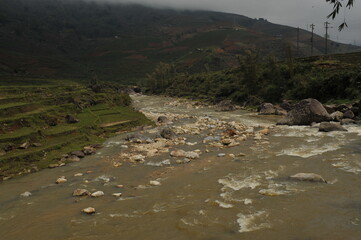 Shallow rock river flowing through rice terraces surrounded by lush green mountain in Sapa, Vietnam.