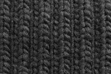Knitted woolen black fabric pattern. Macro texture of a sweater showing woven yarn details
