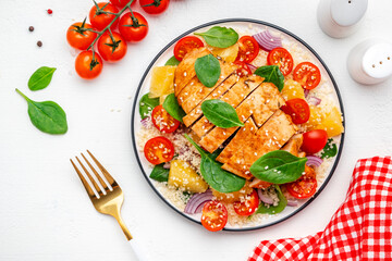 Yummy salad with chicken, couscous, tomatoes, onion, spinach and orange. White table background,...