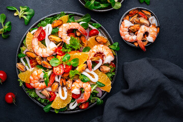 Delicious seafood salad with shrimp, mussels, squid, oranges, lettuce and olive oil with lemon dressing, black background, top view