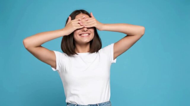 A young woman with a playful smile reveals her eyes after covering them with her hands.
