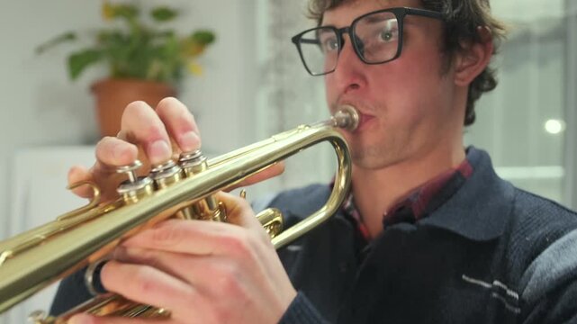 Close-up of a man playing trumpet indoors with puffed cheeks and focused expression. Moment of musical concentration and expression captured in warm indoor lighting.