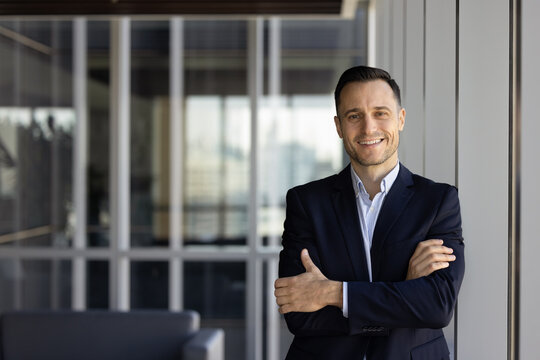 Happy successful young Hispanic company owner man posing in office hall interior with hands folded, looking at camera, smiling. Financial advisor, lawyer, executive portrait with copy space