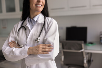 Confident successful happy young female doctor in lab coat and stethoscope standing in clinic...